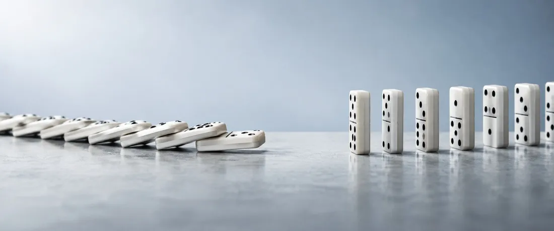 A run of white dominoes toppled from the left, a missing tile in the middle, and the rest still standing on the right.